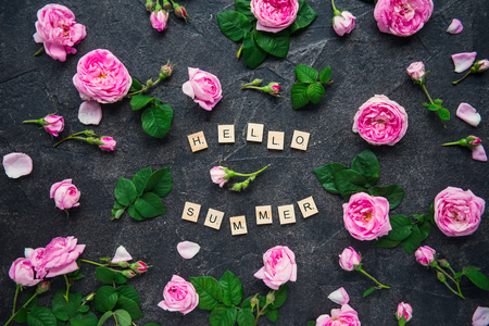 Hello Summer inscription by wooden letters and fresh spring pink tea rose flowers on dark stone background. Lettering summer season. Creative layout design concept. Soft selective focus.の写真素材