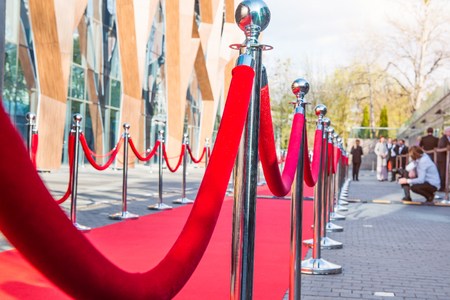 Close up red carpet ceremony with selective focus on the stanchions and the ropes with blurred guests and photographer background. Celebrity lifestyle concept.の写真素材
