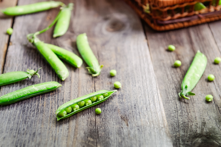 Farmer harvest of fresh green peas on the table and in a woven straw basket on the old rustic wooden background. Top view, selective focus. Space for text.の写真素材