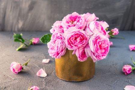 Close up tender pink tea roses bouquet in vintage golden pot on the dark background. Postcard mock up. Summer, spring flowers. Selective focus. Copy spaceの写真素材