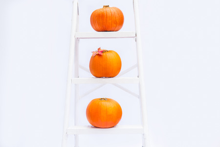 Composition of Three pumpkins with maple leaf on stairs on the steps of croped rung ladder on white background isolated. Autumn holiday, harvest, Helloween concept. Selective focus, Copy spaceの写真素材