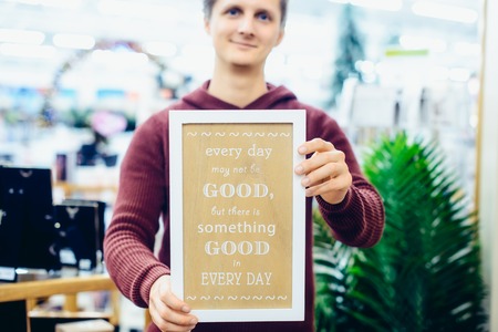 Portrait of Young smiling caucasian man holding motivational message typing on the wooden board....