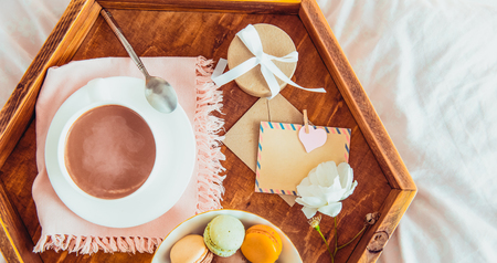 Breakfast in bed with empty blank card for text. Cup of coffee, juice, macaroons, rose flower and giftbox on wooden tray. Romantic breakfast in bed. Birthday, Valentine's day morning. Copy spaceの写真素材