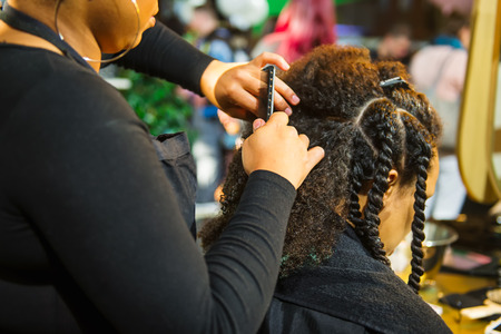 Close up african hairstylist braided hair of afro american female client in the barber salon. Black healthy hair culture and Style. Stylish therapy professional care concept. Selective focusの写真素材