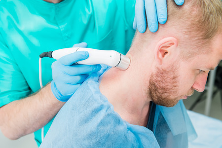 Young man at the physiotherapy receiving laser therapy massage. A chiropractor treats patient's...