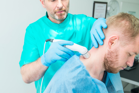 Young man at the physiotherapy receiving laser therapy massage. A chiropractor treats patient's...