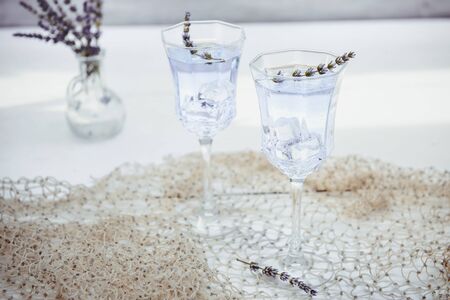 Fresh lavender lemonade with flowers and ice cubes in beautiful glasses on white wooden table. Detox...