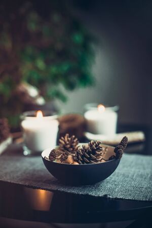 Burning candles and natural decor of cones, nuts in black bowl on the gray fabric napkin on the black table. Cozy atmosphere at home. Kinfolk Hygge Slow Living Style. Dark interior details conceptの写真素材