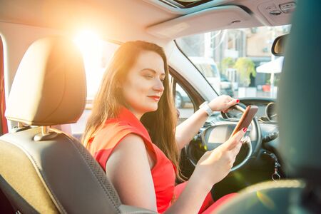 Back view caucasian young woman driver using touch screen smartphone and hand holding steering wheel...