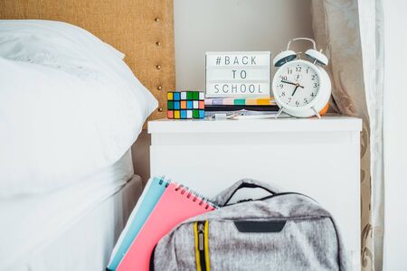 Back to school background. Backback with notebooks near bed and bedside table with lightened box...