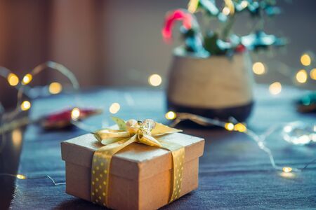 Vintage handcraft gift box with golden ribbon, berry holly in vase and lights garland on gray...