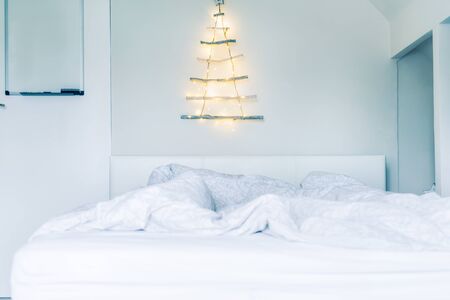 Unusual Christmas tree made of wooden sticks with a garland on the white wall above the bed . Simple, minimal conscientious Christmass interior design. Soft selective focus. Copy spaceの写真素材