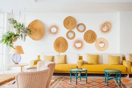 Modern minimal home interior design. Yellow sofa with pillows, green tables, fresh green plants in hanging pots, decorative straw decor, Scandinavian eco natural trendy style. Copy spaceの写真素材