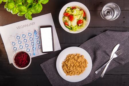 Top view vegetarian and vegan food eating. Healthy dishes - quinoa, fresh vegatable and beetroot salads and dailly veginuary calendar with smartphone on served black wooden table. Day diet planningの写真素材