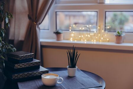 Cup with coffee on black table near window with blurred lighting word Love and home potted flowers on the windowsill. Casual, Hyggehome interior decoration. Romantic mood in noir nordic styleの写真素材