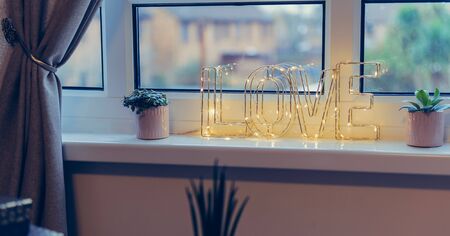 Home interior decoration with wire word Love in lighting garland and home potted flowers on the...