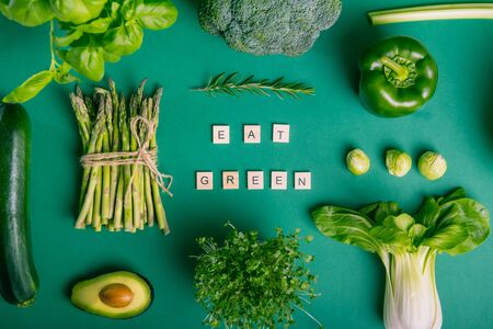 Top view set of healthy raw vegetables on the green background with Eat Green message on wooden...