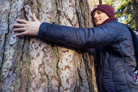 Close up calm and smiling young Nature-Lover man with backpack Hugging a Huge Tree Trunk at the...
