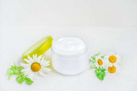 Herbal cosmetic body cream with chamomile oil in opened plastic container and fresh flowers on white background. Natural organic moisturizer and cleansing skincare product. Selective focus. Copy spaceの写真素材