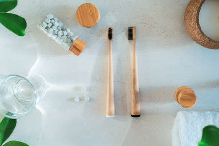Top view zero waste bathroom items. Bamboo toothbrushes, natural mouthwashing tabs, fresh green leaves and glass of water on light background. Oral care essentials. Eco-friendly home. Minimalism.の写真素材