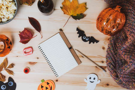 Top view Blank notebook on wooden table with traditional Halloween decor, bats, ghost silhouettes, lighting pumpkin, autumn leaves and warm plaid. Cozy concept of autumn holidays, Flatlay. Copy spaceの写真素材