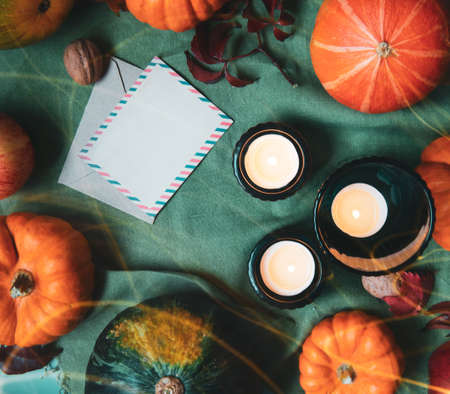 Top view orange and green decorative pumpkins, apples, nuts, candles and blank postcard with envelope in autumn thanksgiving composition on trendy earth tones background. Selective focus. Copy space.の写真素材