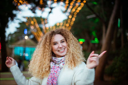 Portrait of Christmas happy smiling blonde curly woman wearing knitted white sweater and dancing or...