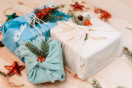 Zero waste christmas concept. Gift boxes wrapped in fabric with spruce branch and berries on wooden background. Flatlay. Eco friendly Sustainable lifestile. No plastic. Selective focus. Copy spaceの写真素材