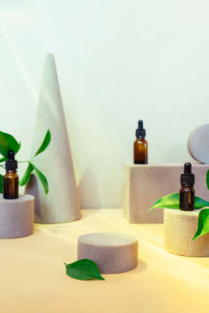 Trendy background of geometric shapes with natural essential oils bottles, fresh leaves and empty central podium for product presentation. Beauty and body care product concept. Sun light and shadows.の写真素材