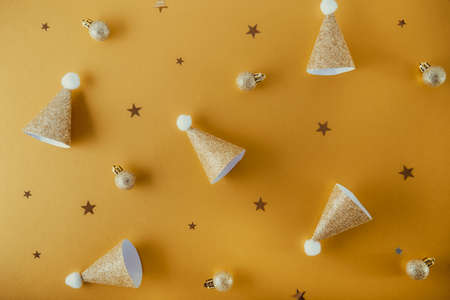 Creative Christmas background in trendy golden color. Festive paper shining caps, small balls and...