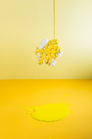 Bright yellow paint is pouring onto the snowflake hanging in the air. Puddle of paint under it. Creative background of the color of the year 2021 announcement. Creative process. Vertical cardの写真素材