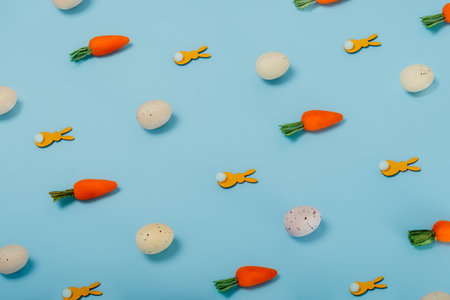 Easter pattern made of colored eggs, decorative carrots, and yellow bunny rabbits on pastel blue...