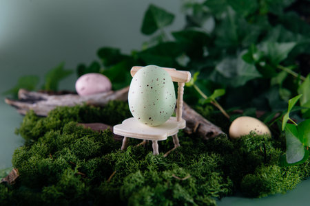 Creative Easter composition of Easter egg on a miniature wooden chair standing in the moss and woods...