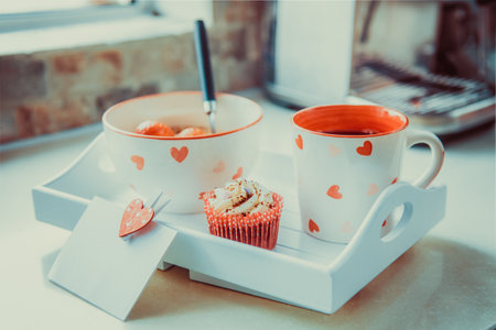 A tray with oatmeal porridge bowl with strawberries, a cup of coffee or tea, cupcake, and blank greeting card. Surprise breakfast for lover on Valentines day. Simple festive healthy food idea.の写真素材