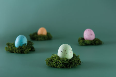 Easter colored eggs laying on the moss pillow on the green background. Happy Easter holiday. Muted colors. Selective focus. Copy space.の写真素材