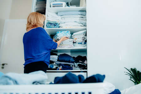 Back view of a woman organizing a wardrobe, holding towels in her hands and putting them on a shelf. Clean up your home space, make your home cozy. Selective focus, copy space.の写真素材