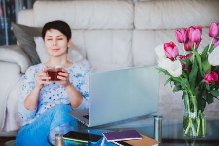 Laptop on a background of a blurred woman drinking a cup of tea and enjoying the moment on her...