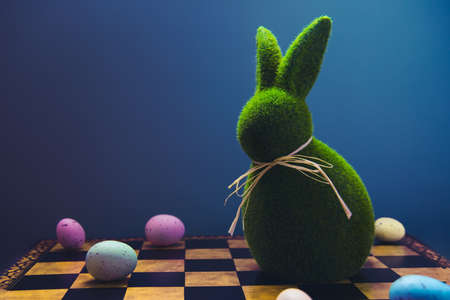 Creative and trendy Easter concept. Easter chess play with colored eggs and Easter green bunny rabbit on the dark blue background. Selective focus, copy space.の写真素材