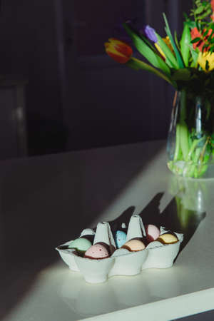 Easter celebration minimalism concept. Pastel colors painted eggs in a cardboard box and fresh...