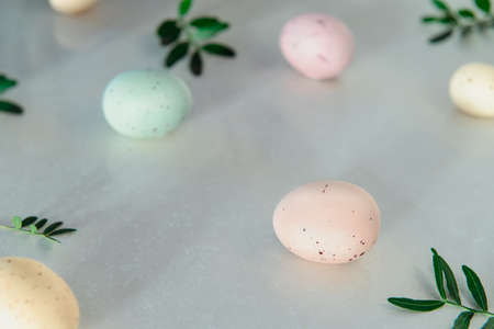 Easter holiday concept. Pastel colors painted eggs with small fresh green leaves on white...
