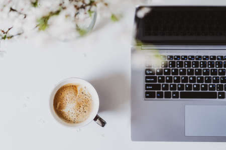 Top view workplace. White office table desk with a cup of fresh coffee, open laptop with keyboard...