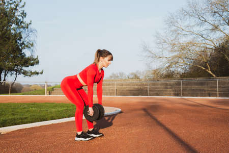 Young fitness woman in red sportswear doing workout sessions outdoor in the stadium. Athlete woman...