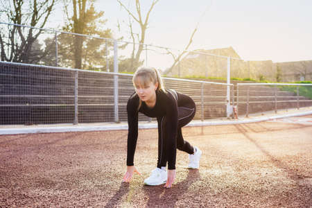 Woman getting ready to start running on stadium. Outdoors workout. Jogging in the stadium. Sunset...