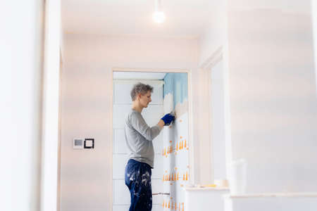 Young man installing wall tile at home. Proffesional tiler laying tiles on a bathroom wall. DIY, Do it yourself concept. House improvement. Repair renovation work. Selective focus, copy spaceの写真素材