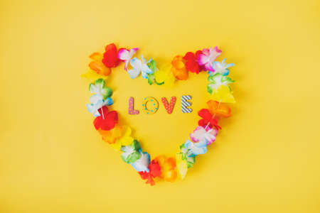 Hawaiian flower necklace in the shape of heart with word Love inside on the yellow background. Summer background. LGBT concept with rainbow flag colors. Selective focus. Copy space.の写真素材