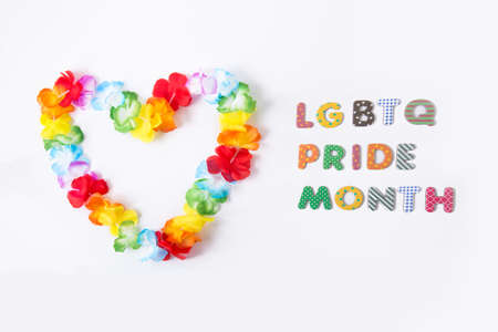 Hawaiian flower necklace in the shape of a heart with LGBTQ Pride month inscription on the white background. LGBT concept with rainbow flag colors. Selective focus. Copy spaceの写真素材