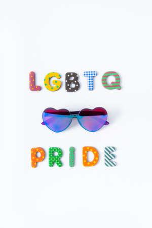 LGBTQ Pride colorful inscription with heart-shaped sunglasses on the white background. Vertical card. LGBTQ concept with rainbow flag colors. Pride month. Selective focus. Copy spaceの写真素材