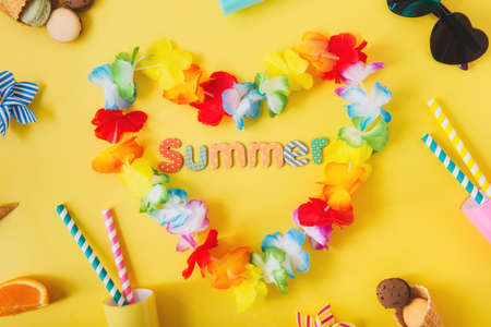 Top view flat lay of Hawaii flower necklaces in shape of heart with Summer word, cocktail glasses with straws, sunglasses, waffle cones, macaroon cakes, orange slices on yellow background. party mood.の写真素材