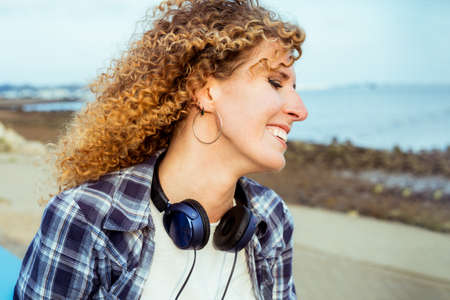 Close up smiling curly hair caucasian woman with large headphones walking outdoor. Enjoy the moment and music. Freedom and happiness, simple pleasures concept.の写真素材