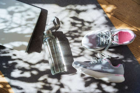 Laptop, sneakers and water bottle on a gray yoga mat background with direct sunlight and shadows. Online Fitness program, Home workout. Workout essentials. Top view, flat layの写真素材